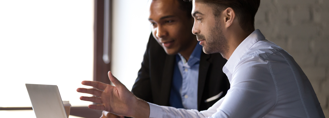 Two management consultants in Calgary discussing a project while looking at a laptop.