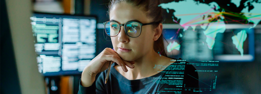 A female IT professional wearing glasses looking at computer screens in an office in Regina.